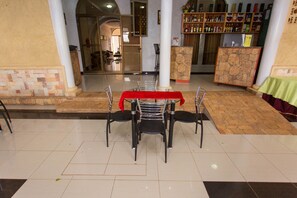 A dining area with a table set for four, surrounded by chairs, a red tablecloth, and a stone pillar.