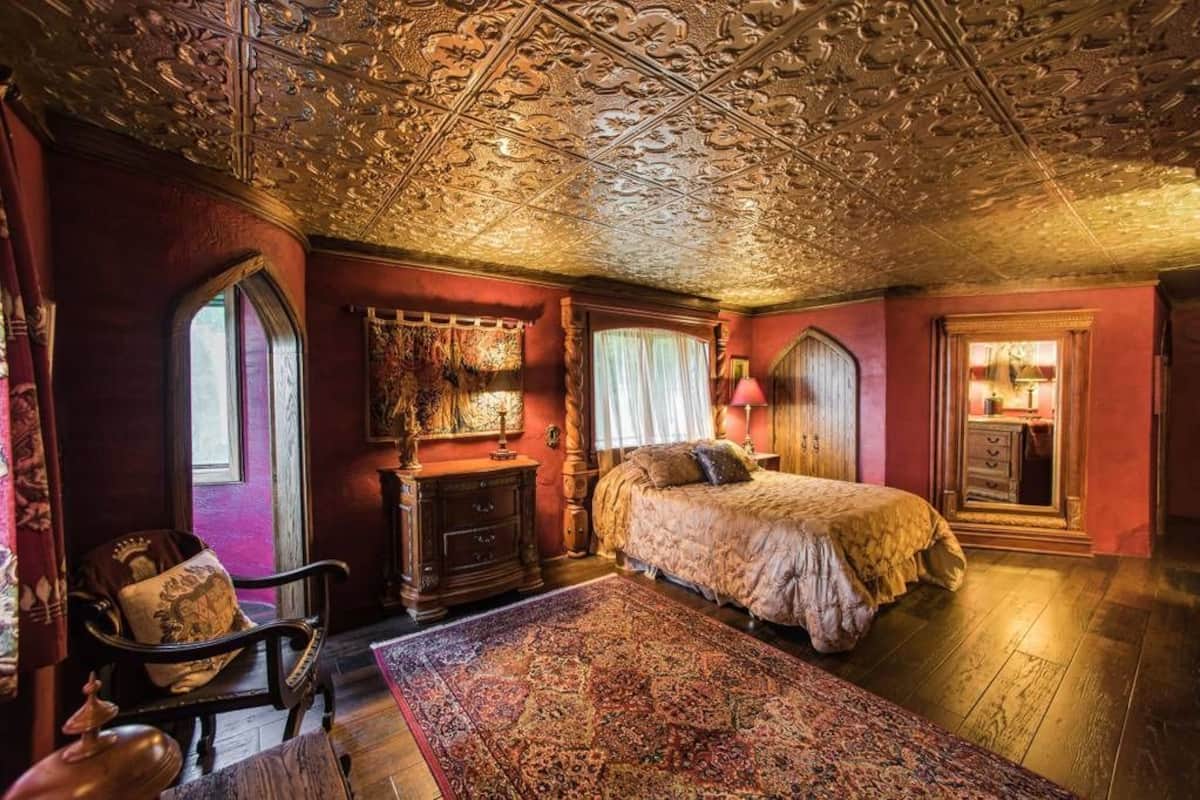 A room with a large bed, ornate ceiling, and a vintage chair.