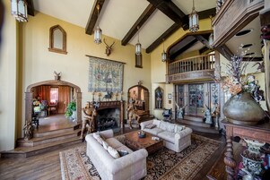 A spacious living room with a fireplace, wooden beams, and a large tapestry.