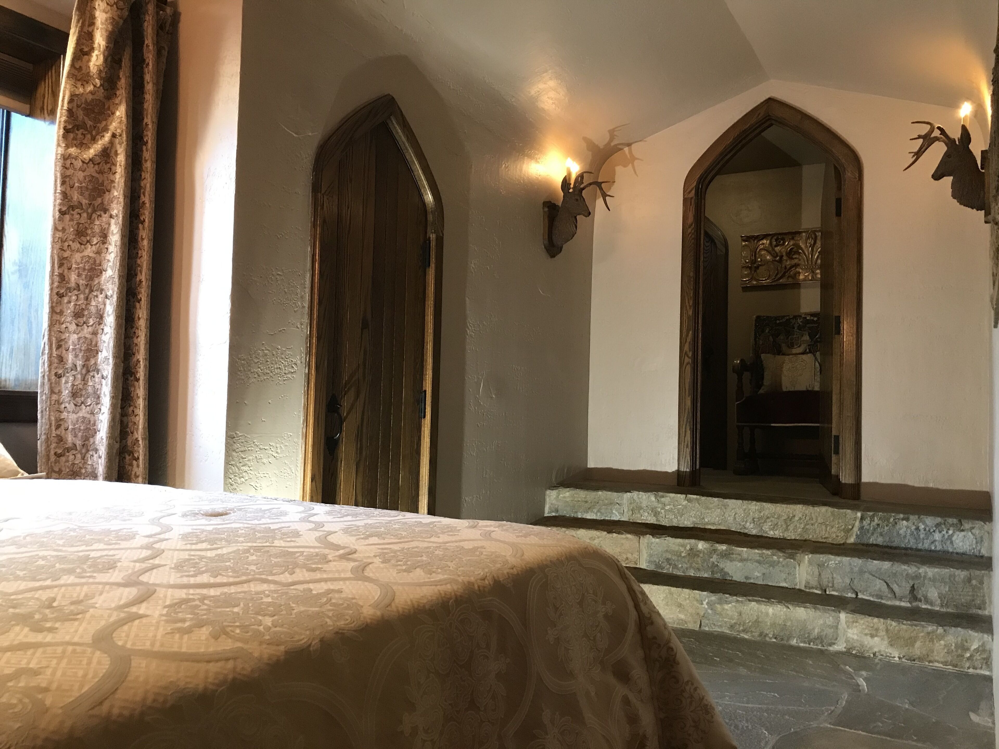 A bedroom with a large bed, a wooden door, and a stone staircase leading to a bedroom.
