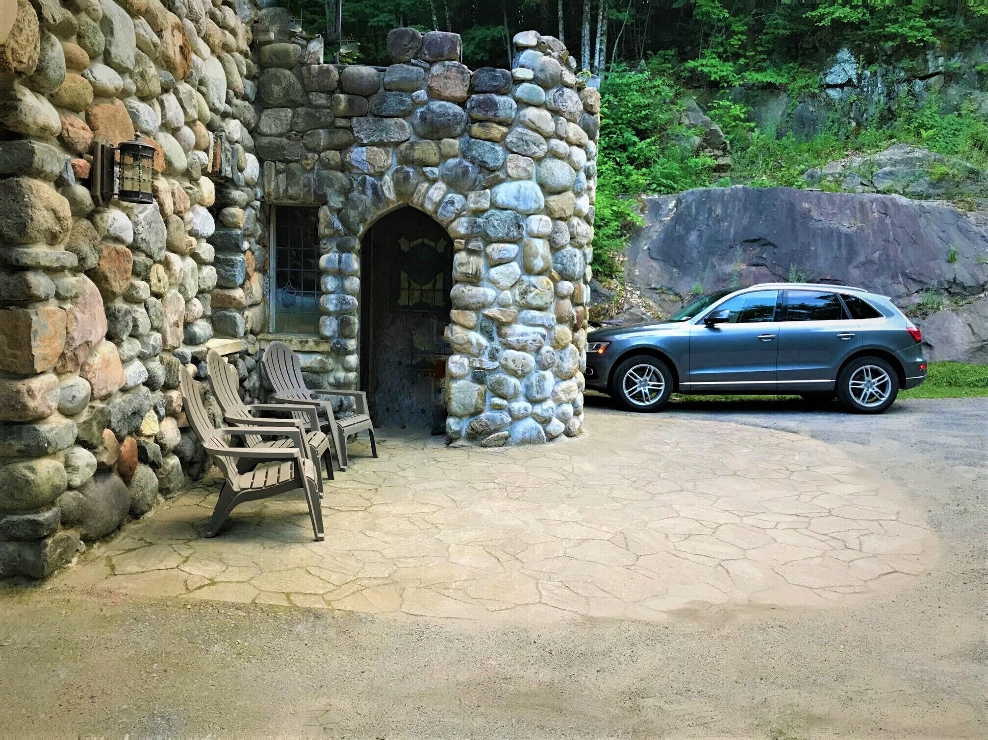 A stone building with a carport, outdoor seating, and a large rock formation in the background.