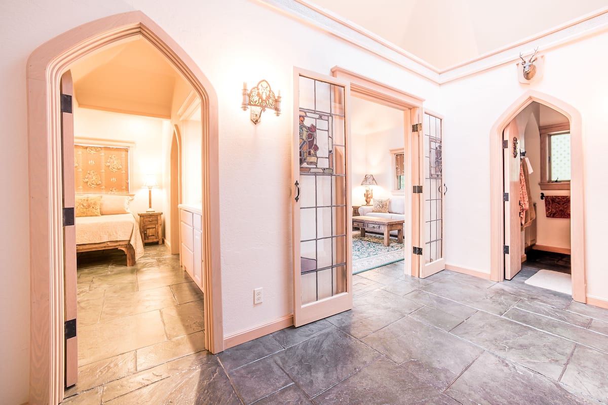 A hallway with a bed, a nightstand, and a lamp. There are two doors with glass panels and a decorative wall light.