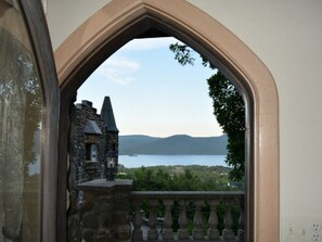 A stone building with a balcony, overlooking a body of water and distant mountains.