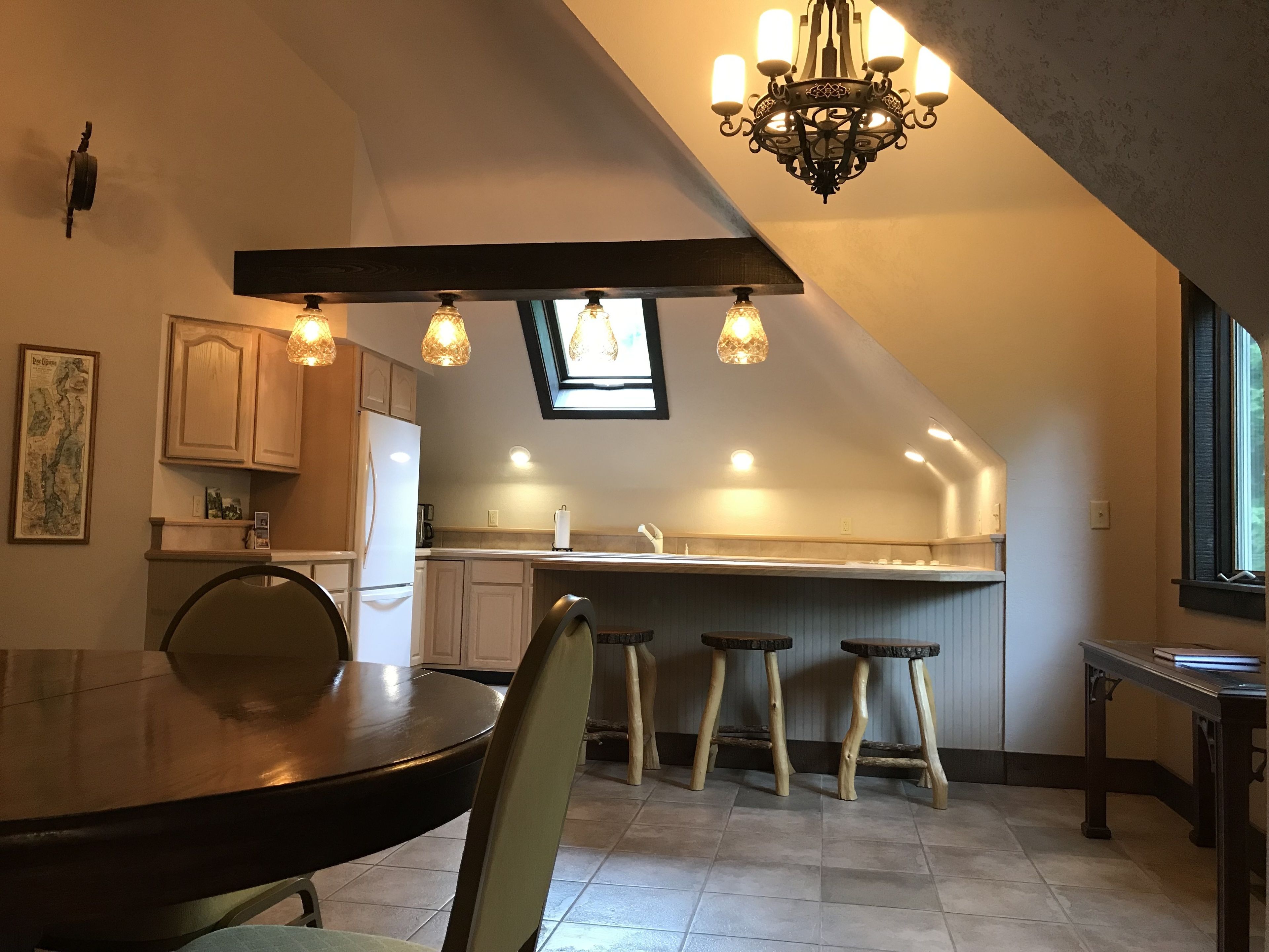 A modern kitchen with a dark wooden table, bar stools, and a chandelier.