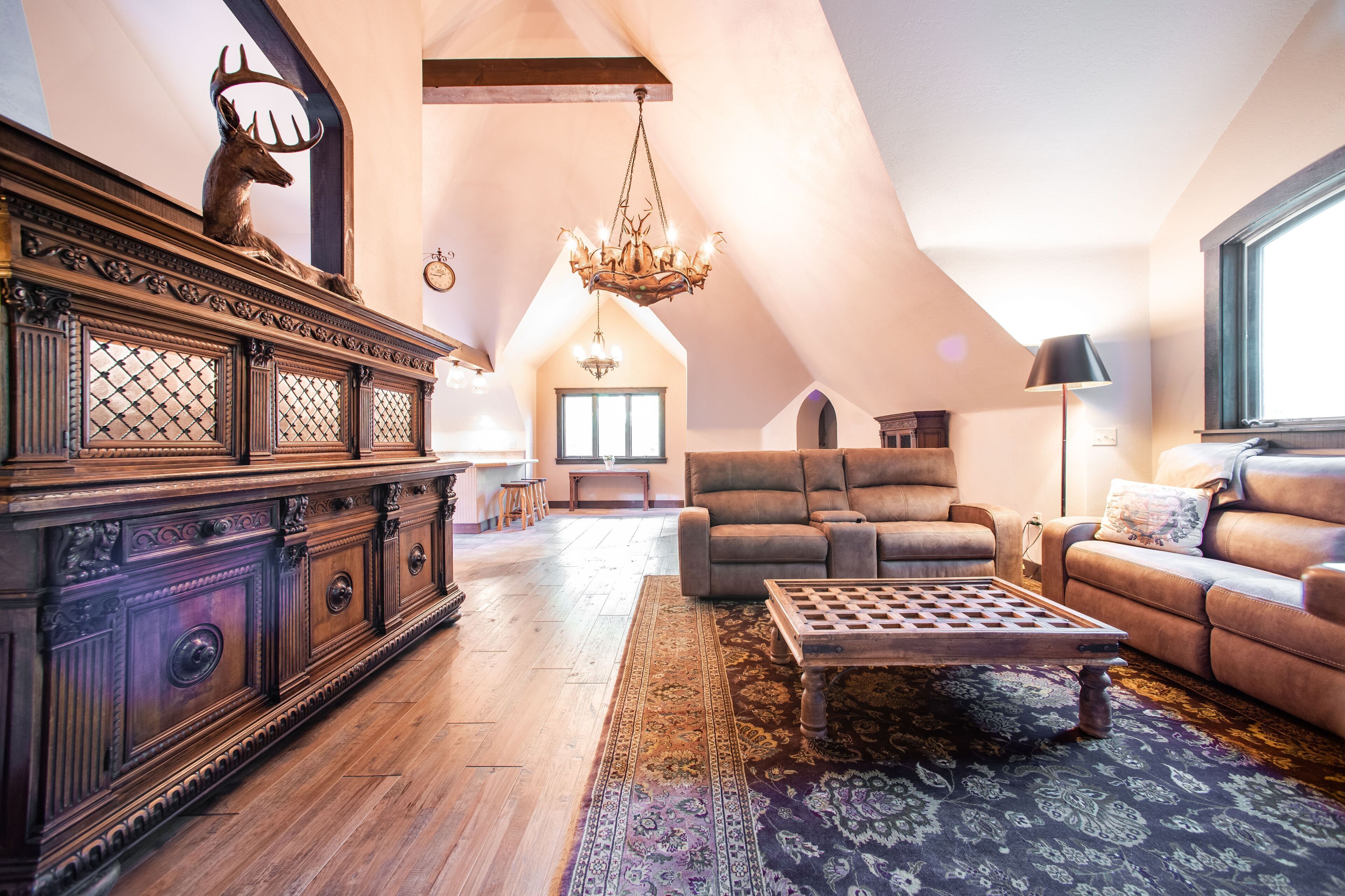 Ein geräumiges Wohnzimmer mit hoher Decke, einem Holztisch, einer Couch und einem großen Spiegel mit Hirschgeweih.