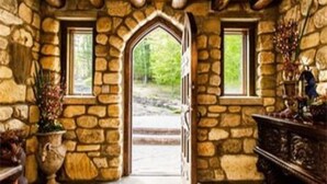 A stone-walled room with a wooden ceiling, a large arched doorway, and a view of a forested area outside. - HIGHLANDS CASTLE overlooking Lake George.. plus 2 other Castles! (Bolton Landing)