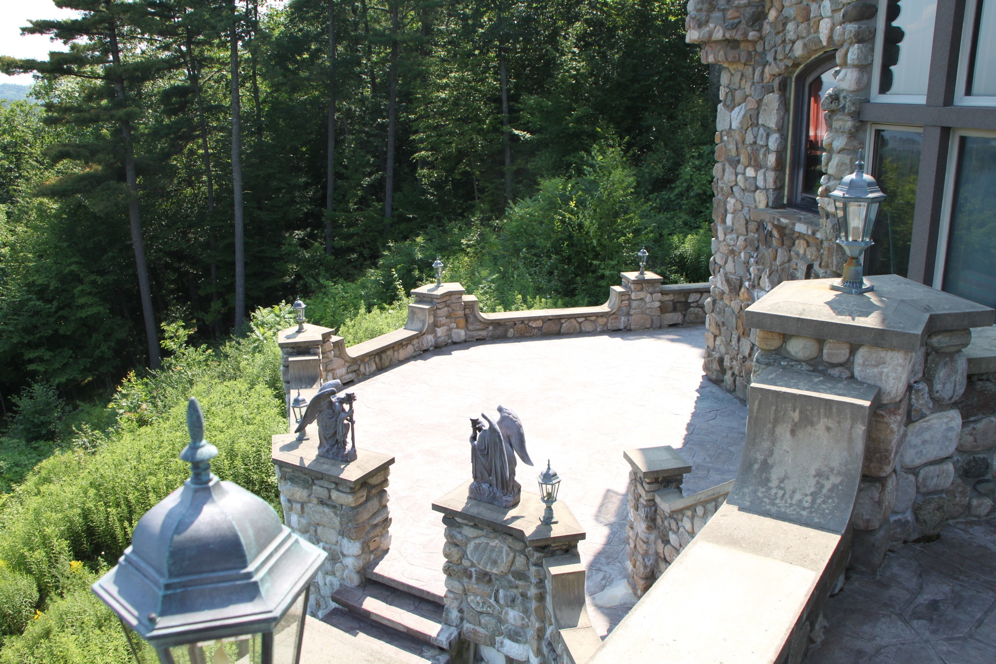 A stone patio with statues and a lantern, surrounded by lush greenery.