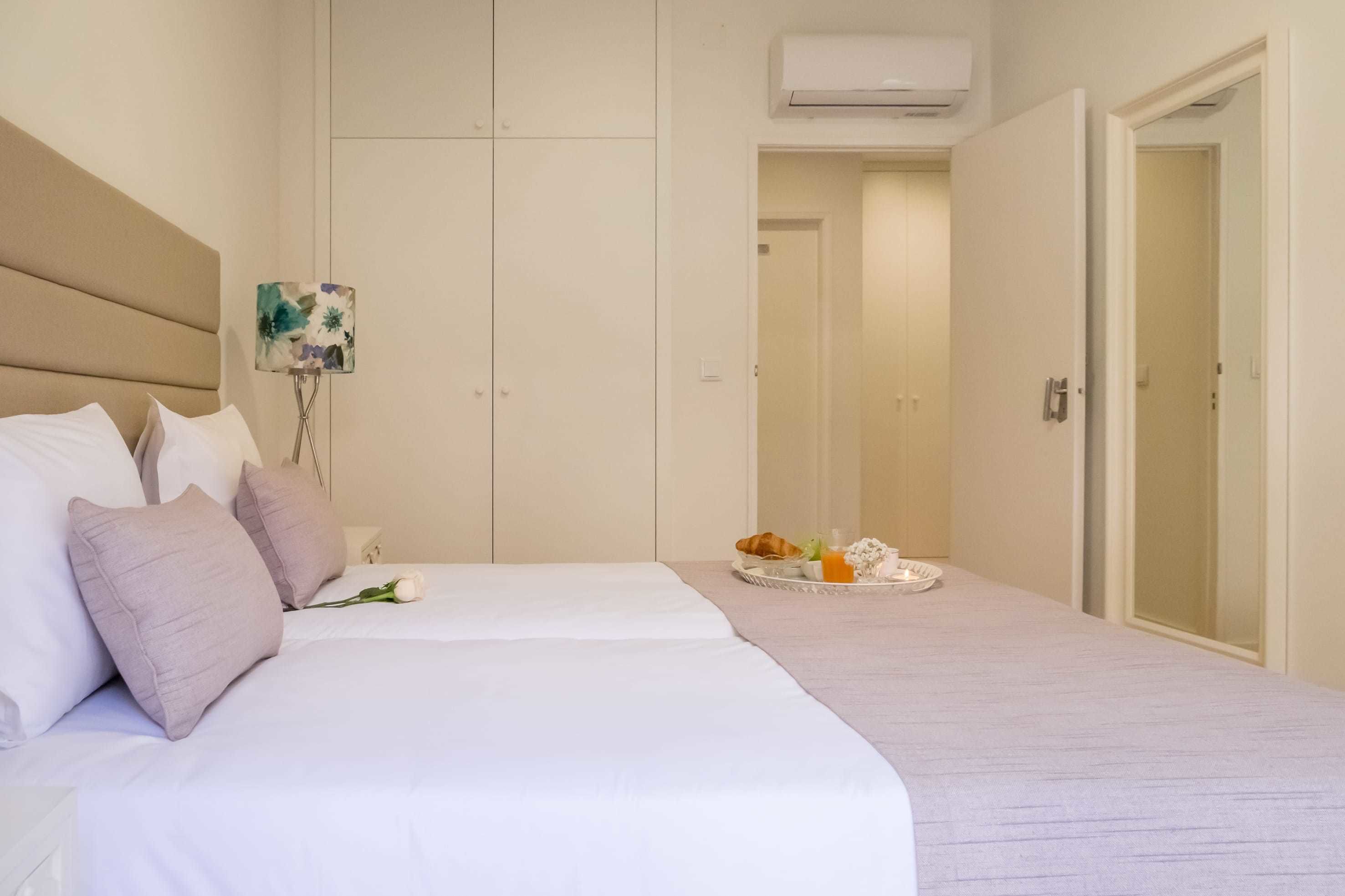 A hotel room with a large bed, a bedside table with a tray of breakfast items, and a door leading to another room.