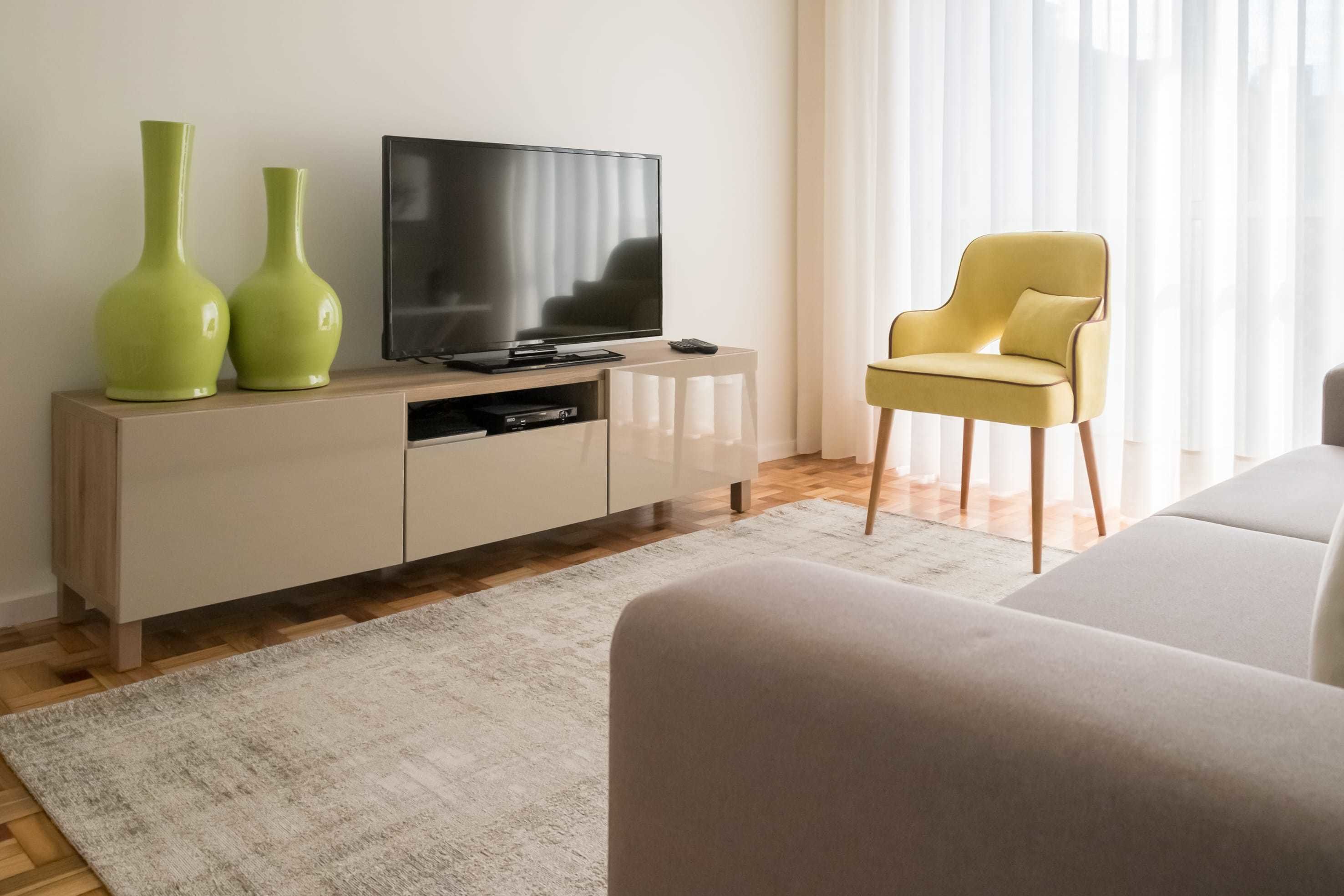 Un salon moderne avec un téléviseur à écran plat, deux vases verts, un fauteuil jaune et un canapé beige.