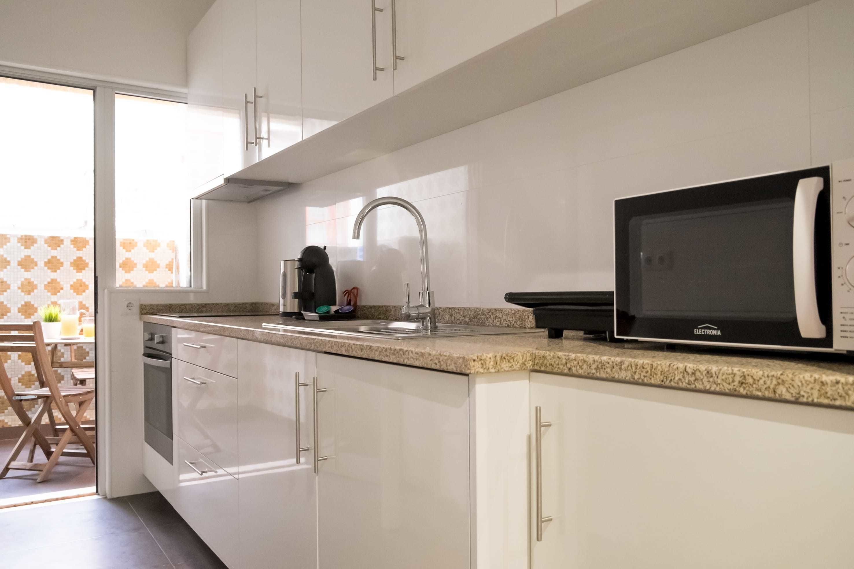 A modern kitchen with white cabinets, a granite countertop, a built-in microwave, and a coffee maker.