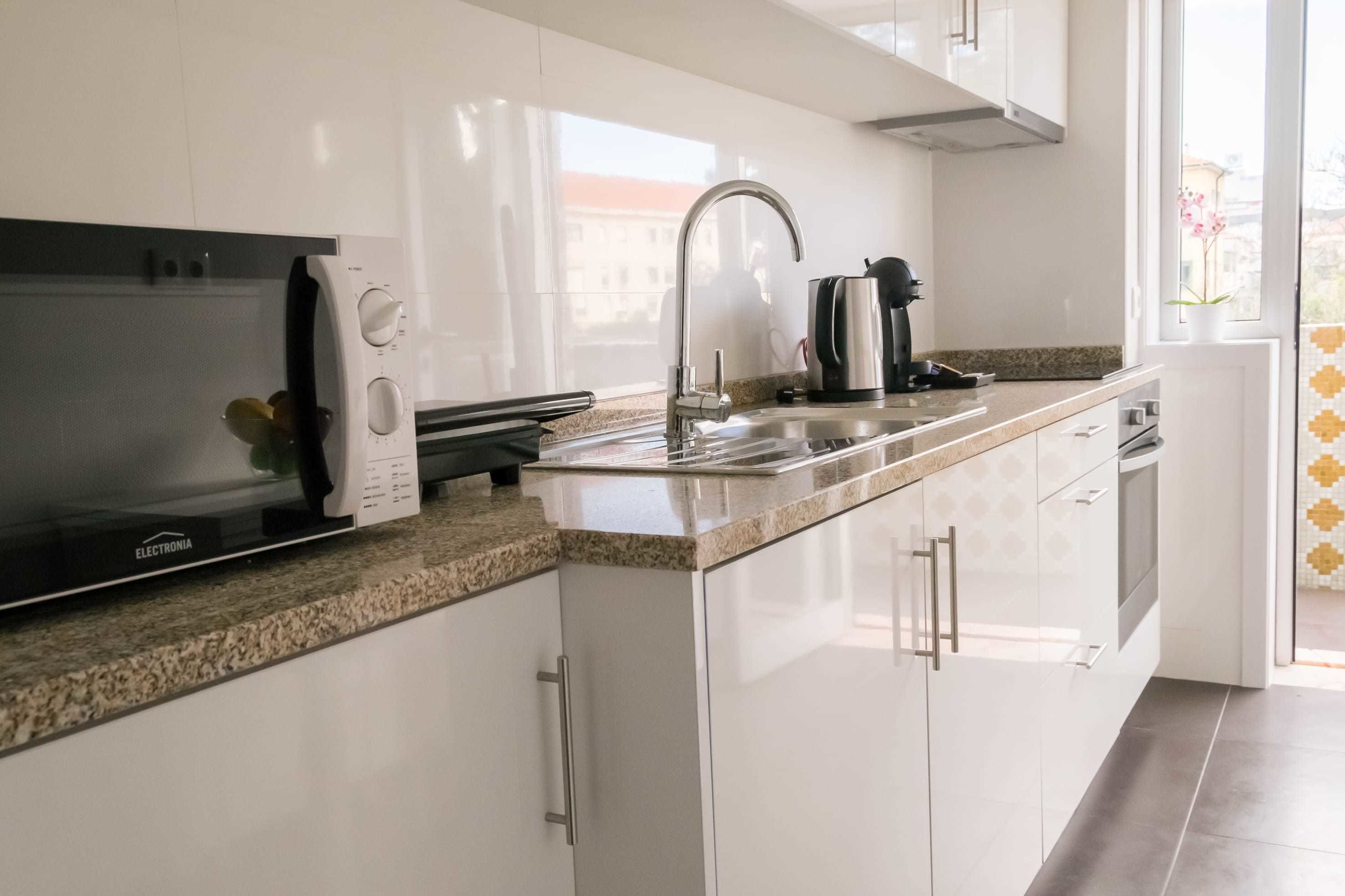 Una cocina moderna con armarios blancos, un lavamanos de acero inoxidable y un microondas integrado.