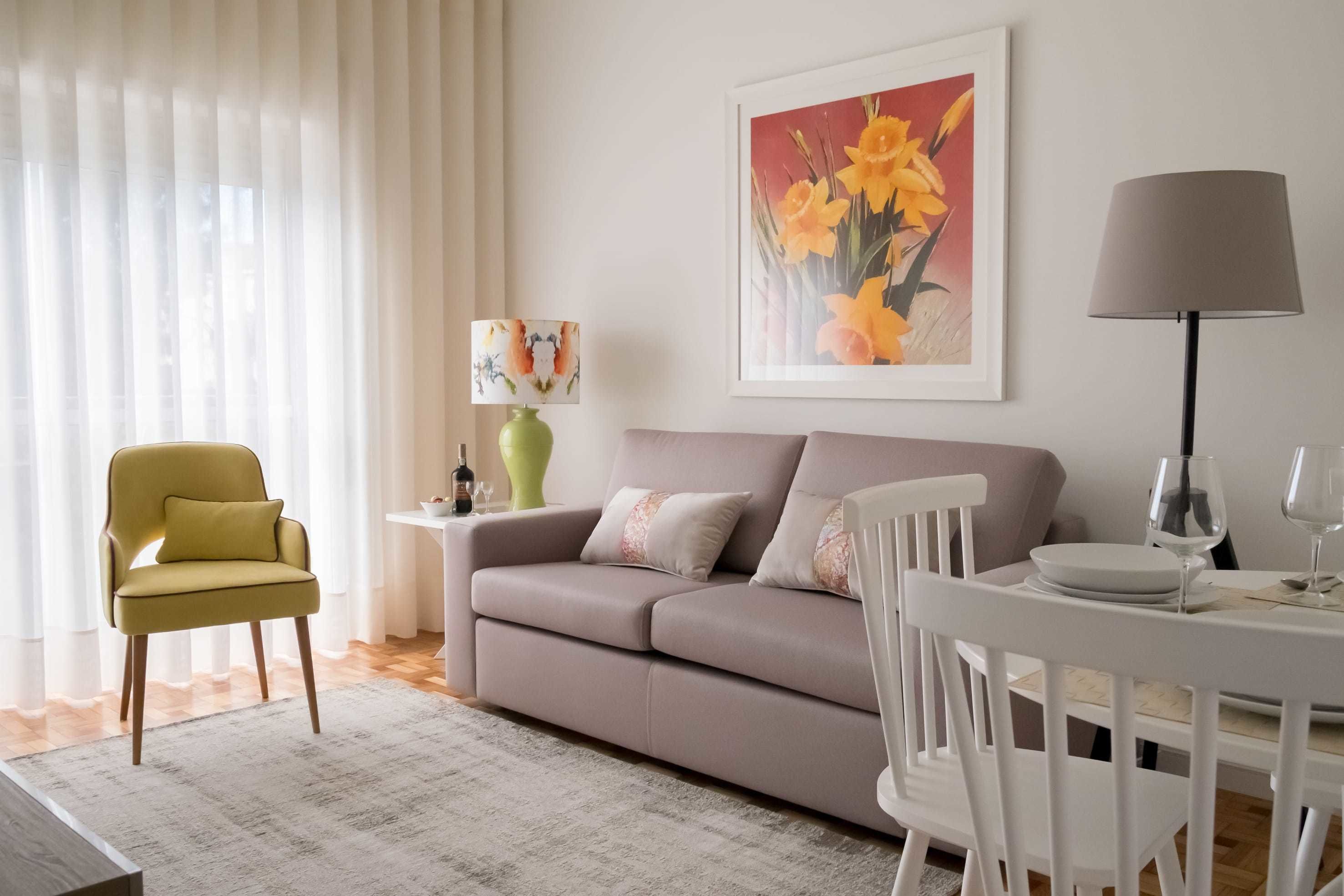 Ein Wohnzimmer mit einer Couch, einem Esstisch mit Stühlen, einer Lampe und einem Bild an der Wand.