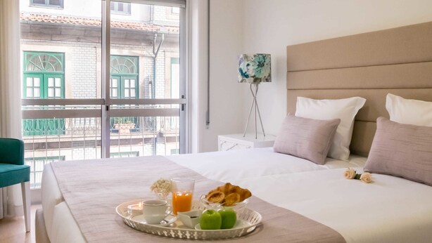 Cama bem arrumada com uma bandeja de itens de café da manhã, mesa de cabeceira e vista para uma varanda com grades verdes.