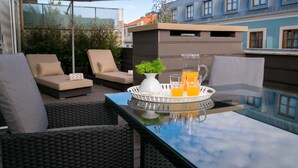 Uma área externa com assentos de vime, uma mesa de vidro e um tabuleiro com bebidas e um vaso.