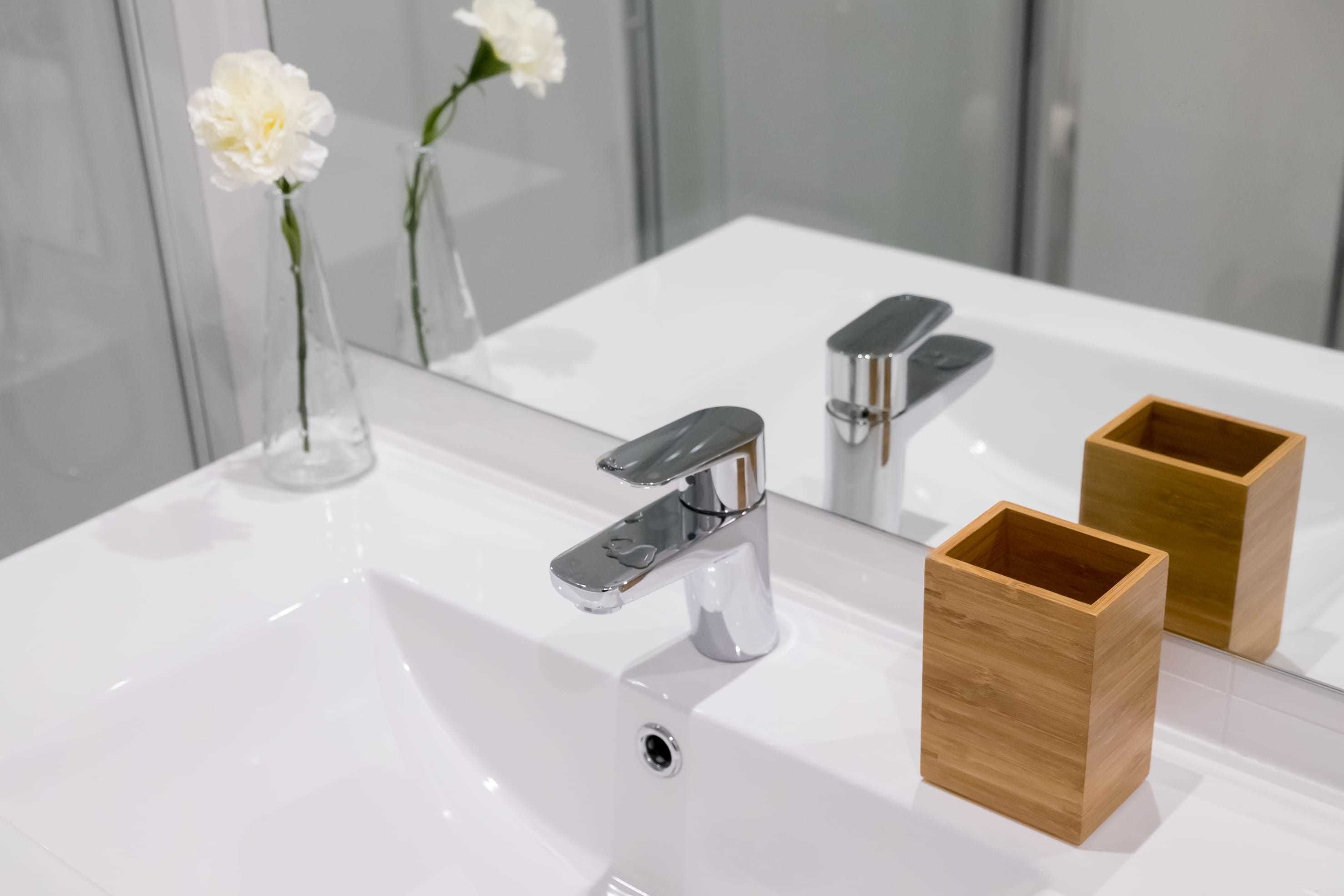 A bathroom with a white sink, chrome faucet, and a wooden container.
