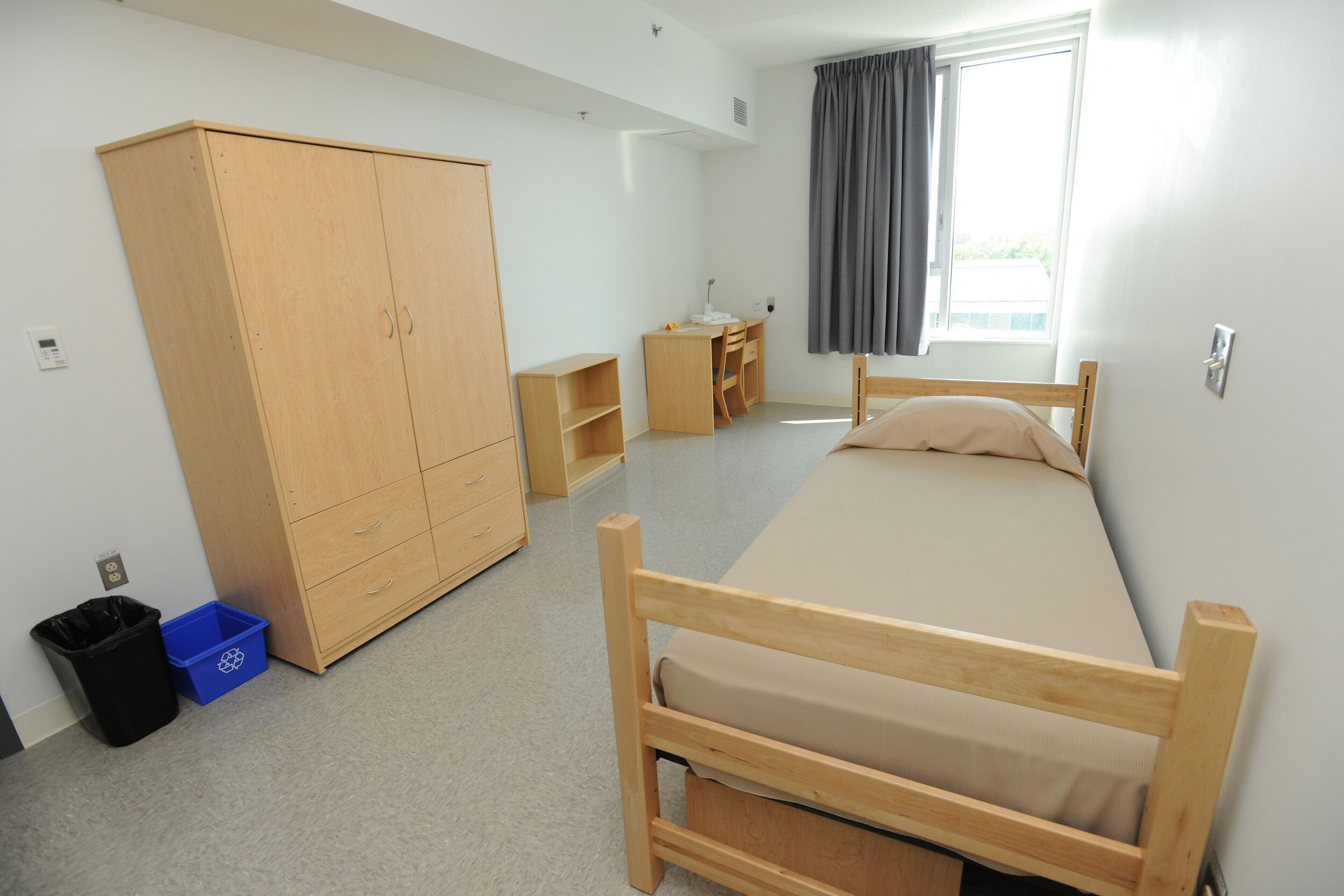 Ein Schlafzimmer mit Bett, Kleiderschrank, Schreibtisch und einem Fenster mit Vorhängen.