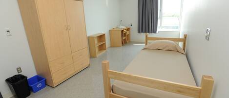 Ein Schlafzimmer mit Bett, Kleiderschrank, Schreibtisch und einem Fenster mit Vorhängen.