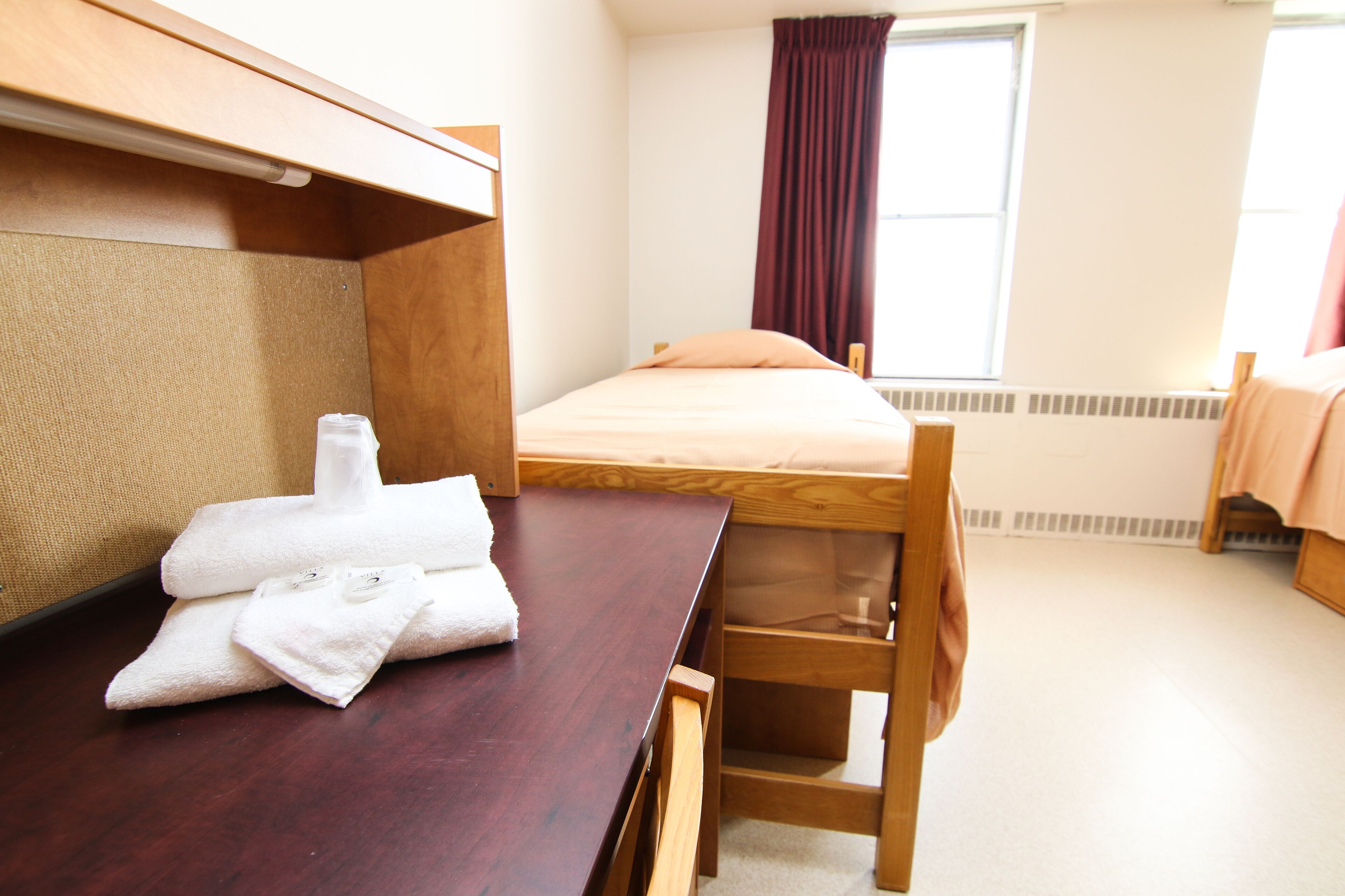 Una habitación de hotel con literas, un escritorio de madera con una silla, una mesita y una ventana con cortinas.