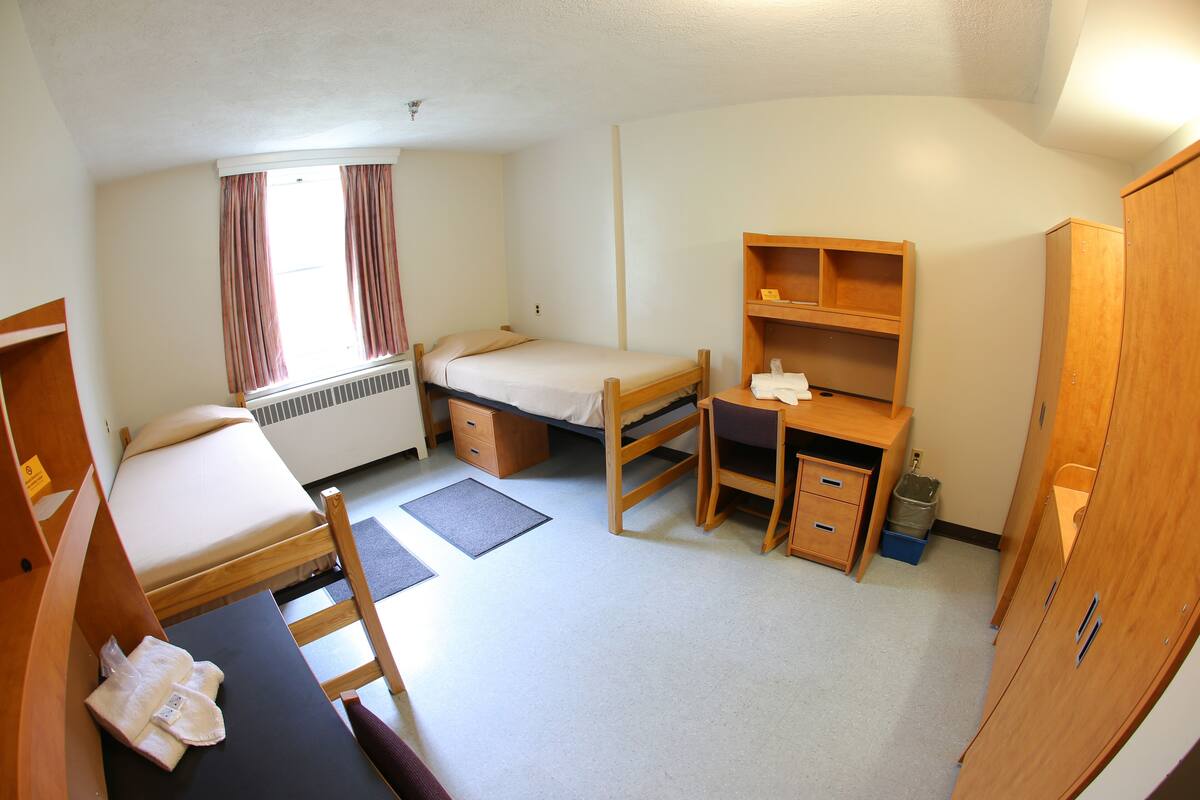 A compact room with a single bed, a desk with a chair, a wardrobe, and a small window with curtains.