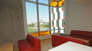 A modern interior with red seating, a white table, and large windows offering a view of a building and a field. - Dalhousie University Accommodations (Halifax)