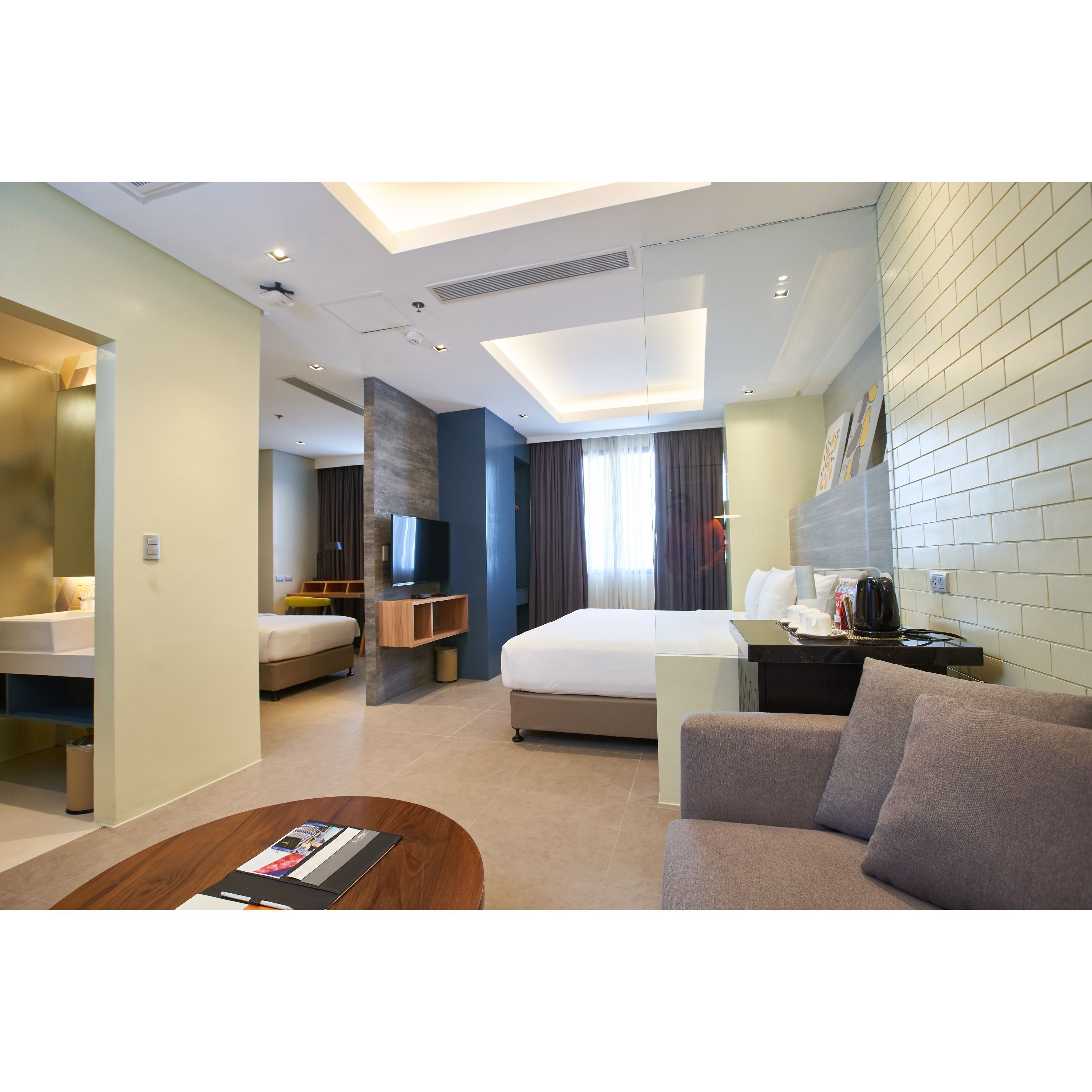 A modern hotel room with a bed, a sofa, a TV, and a small kitchenette.