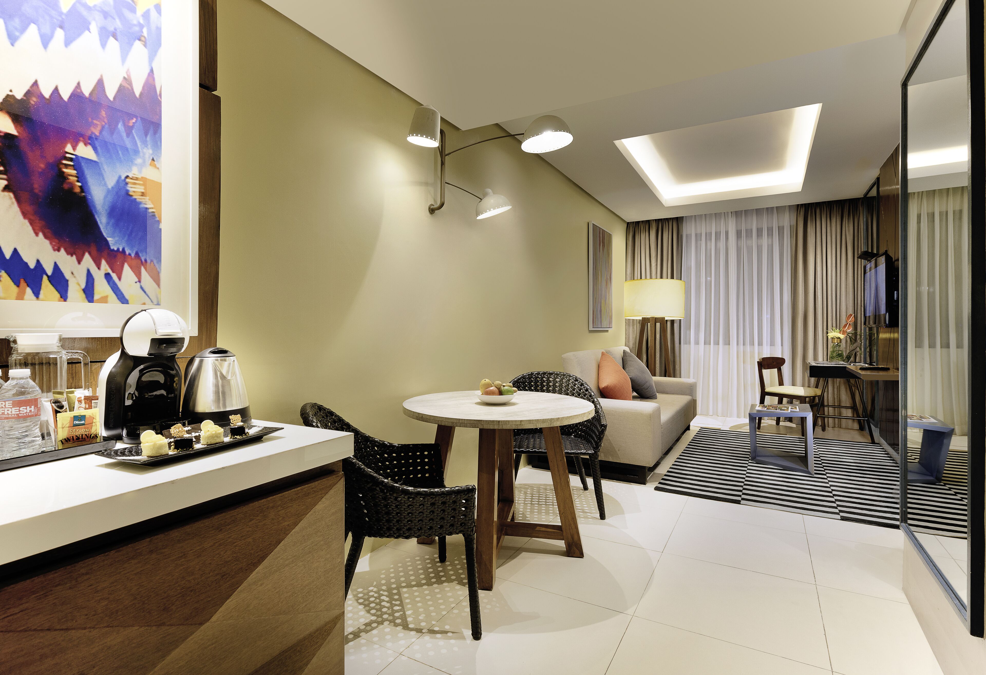 Habitación de hotel con comedor, sofá, máquina de café y un cuadro en la pared.
