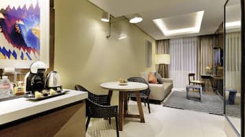 Habitación de hotel con comedor, sofá, máquina de café y un cuadro en la pared.
