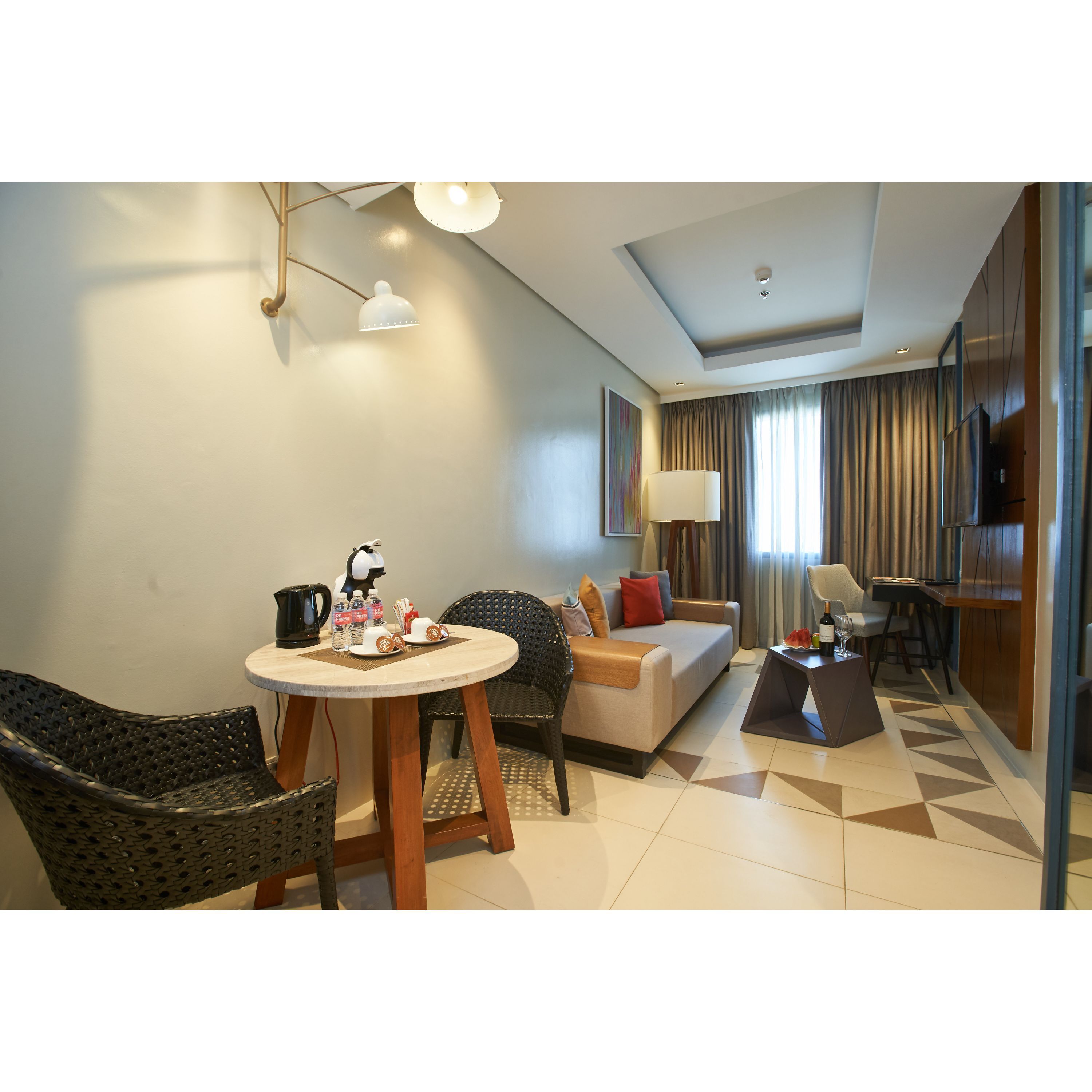 A modern hotel room with a sofa, dining table, chairs, and a TV.