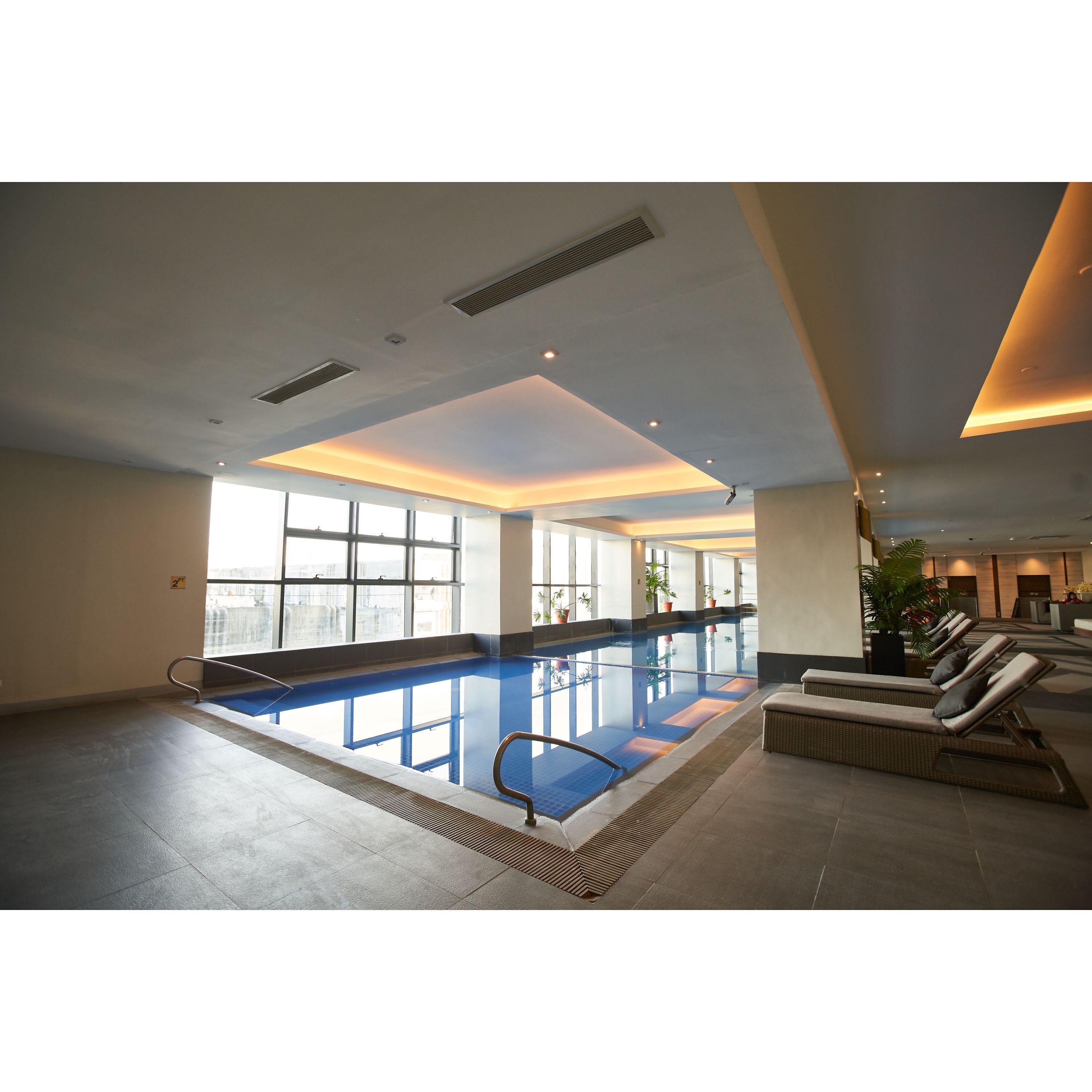 Una amplia piscina interior con agua cristalina y azul, rodeada de sillones de descanso y plantas en macetas.