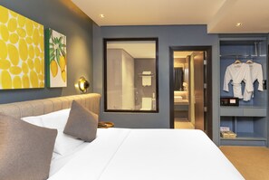 A modern hotel room with a large bed, a wardrobe with hanging robes, and a bathroom visible through a glass door. - Summit Galleria Cebu (Cebu City)