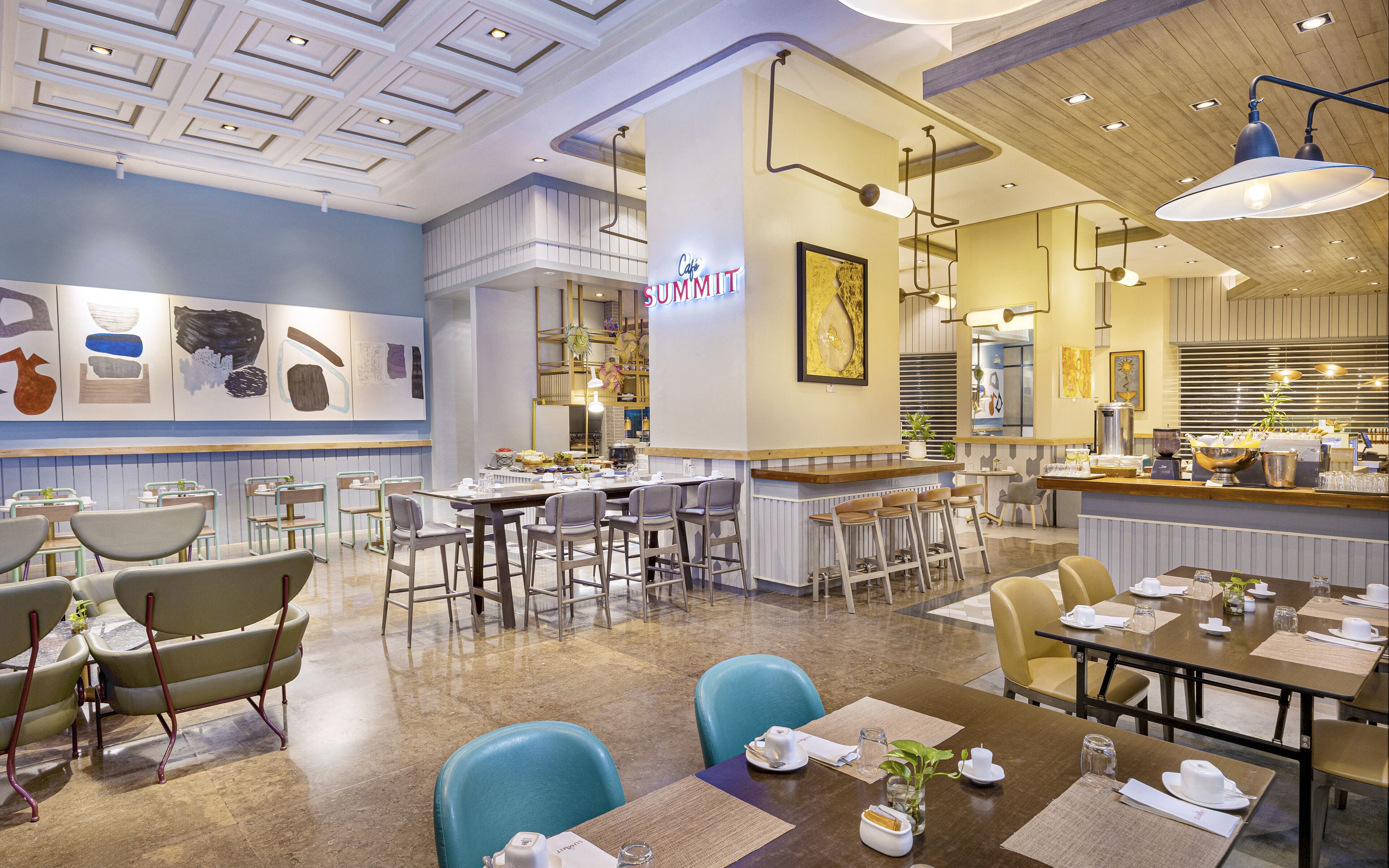 A modern restaurant with a bar area, multiple seating options including bar stools and tables, and a variety of artwork on the walls.
