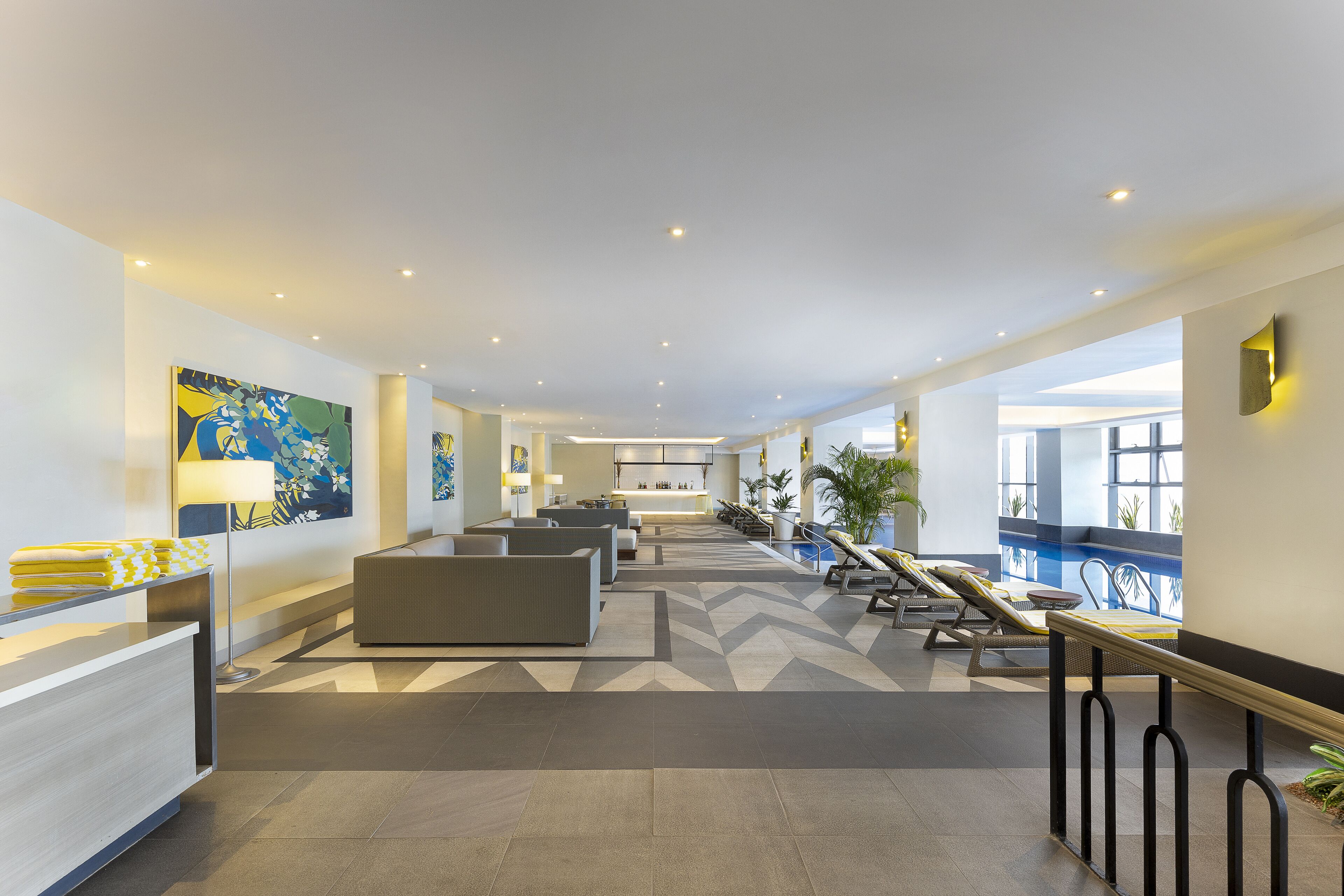 A spacious lobby with a reception desk, seating area, and a pool area with loungers.