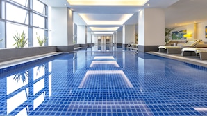 A large indoor swimming pool with clear glass walls, a tiled floor, and a seating area with cushions and a lamp. - Summit Galleria Cebu (Cebu City)