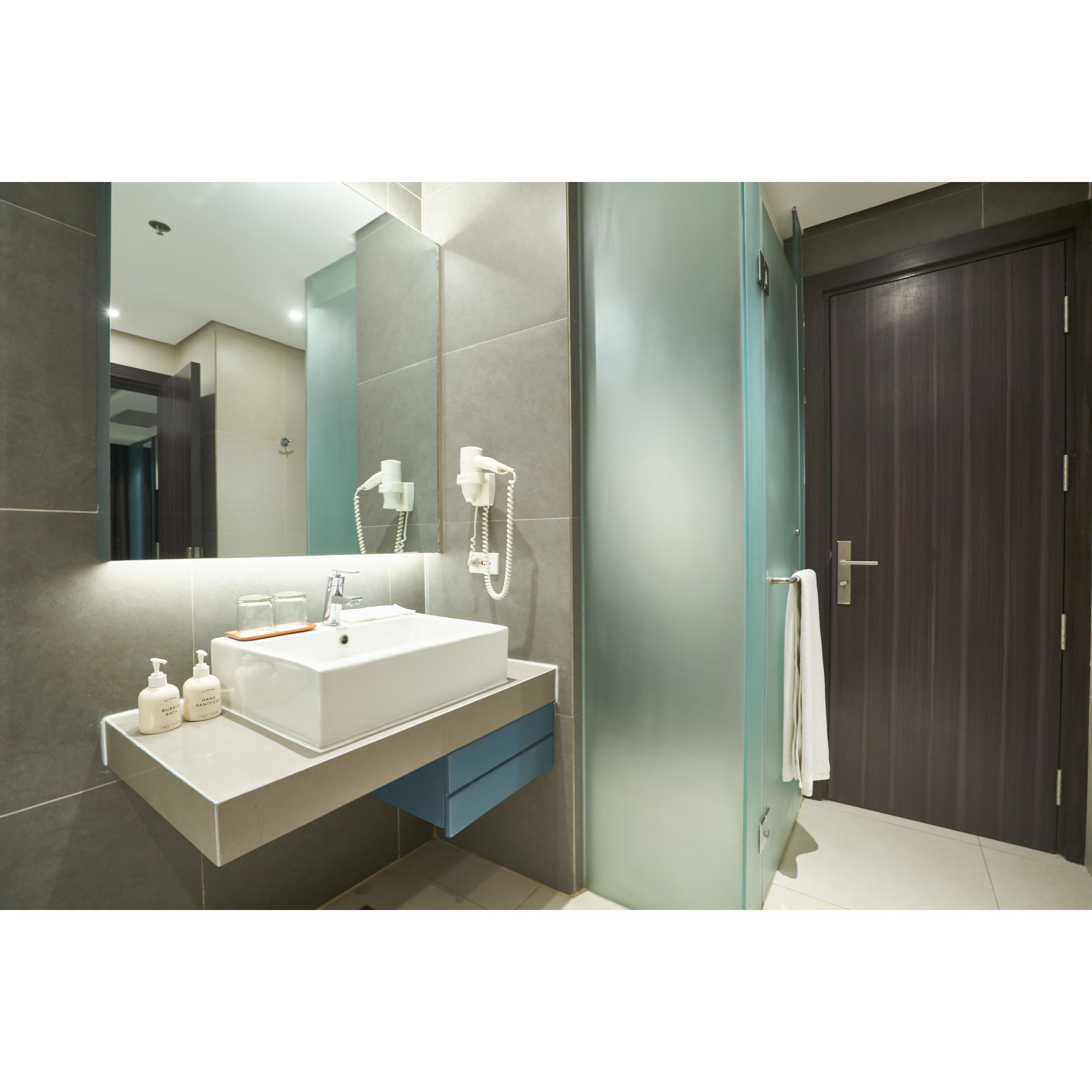 A modern bathroom with a large mirror, a white sink, and a towel hanging on the door.