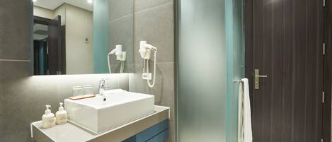 A modern bathroom with a large mirror, a white sink, and a towel hanging on the door.