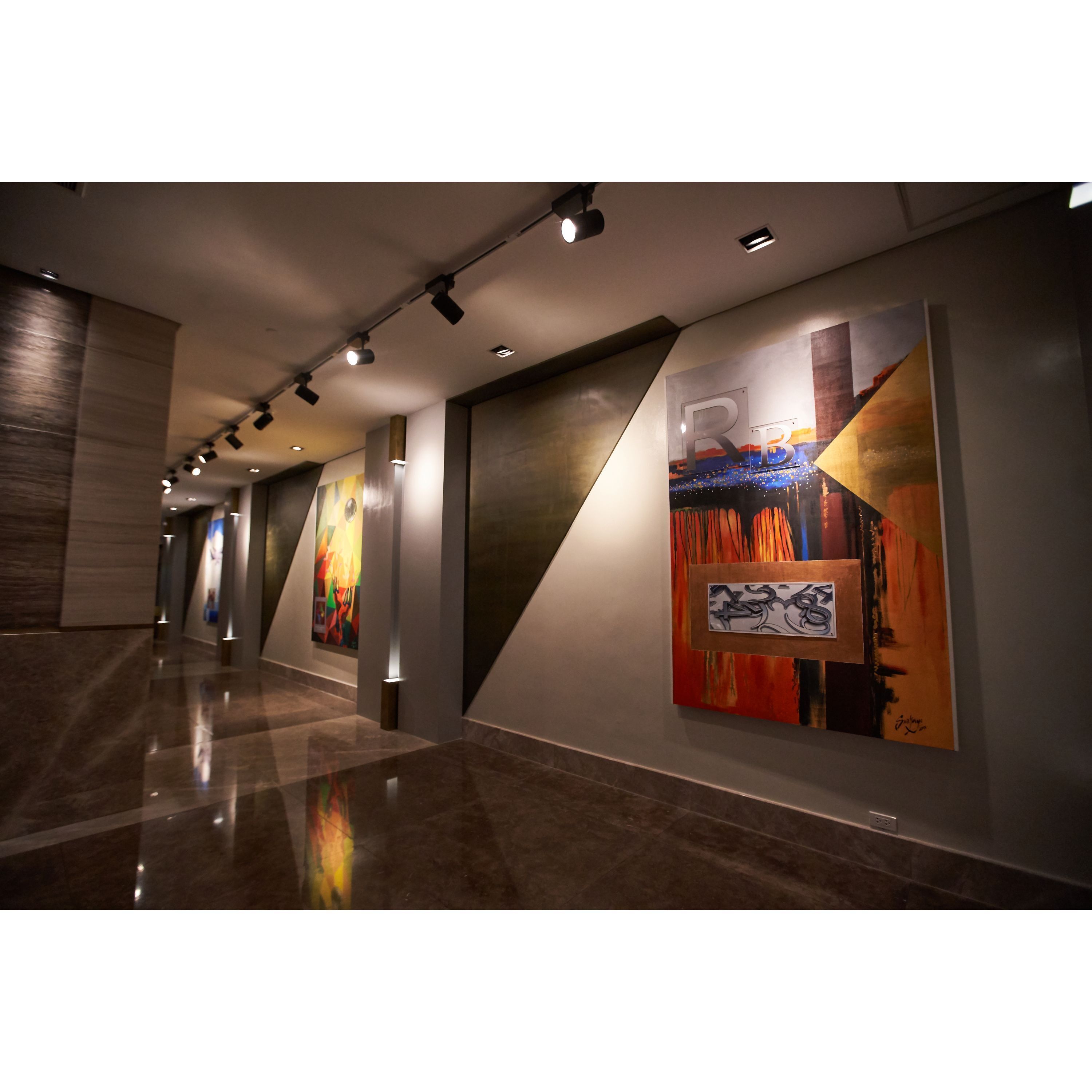 Un couloir moderne agrémenté d’œuvres d’art murales, d’un éclairage encastré et d’un plancher poli.