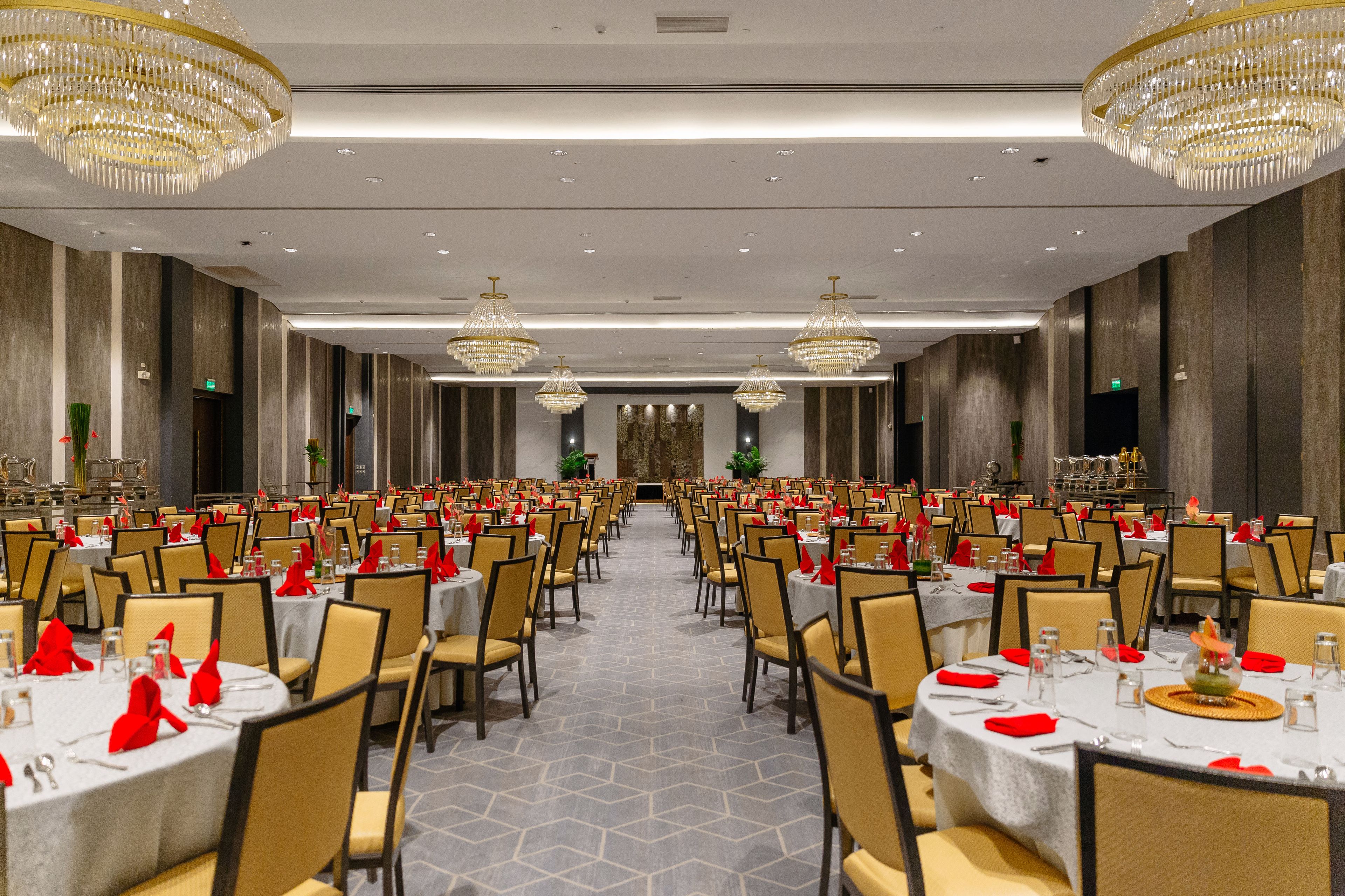 A banquet hall with round tables, chairs, and chandeliers.