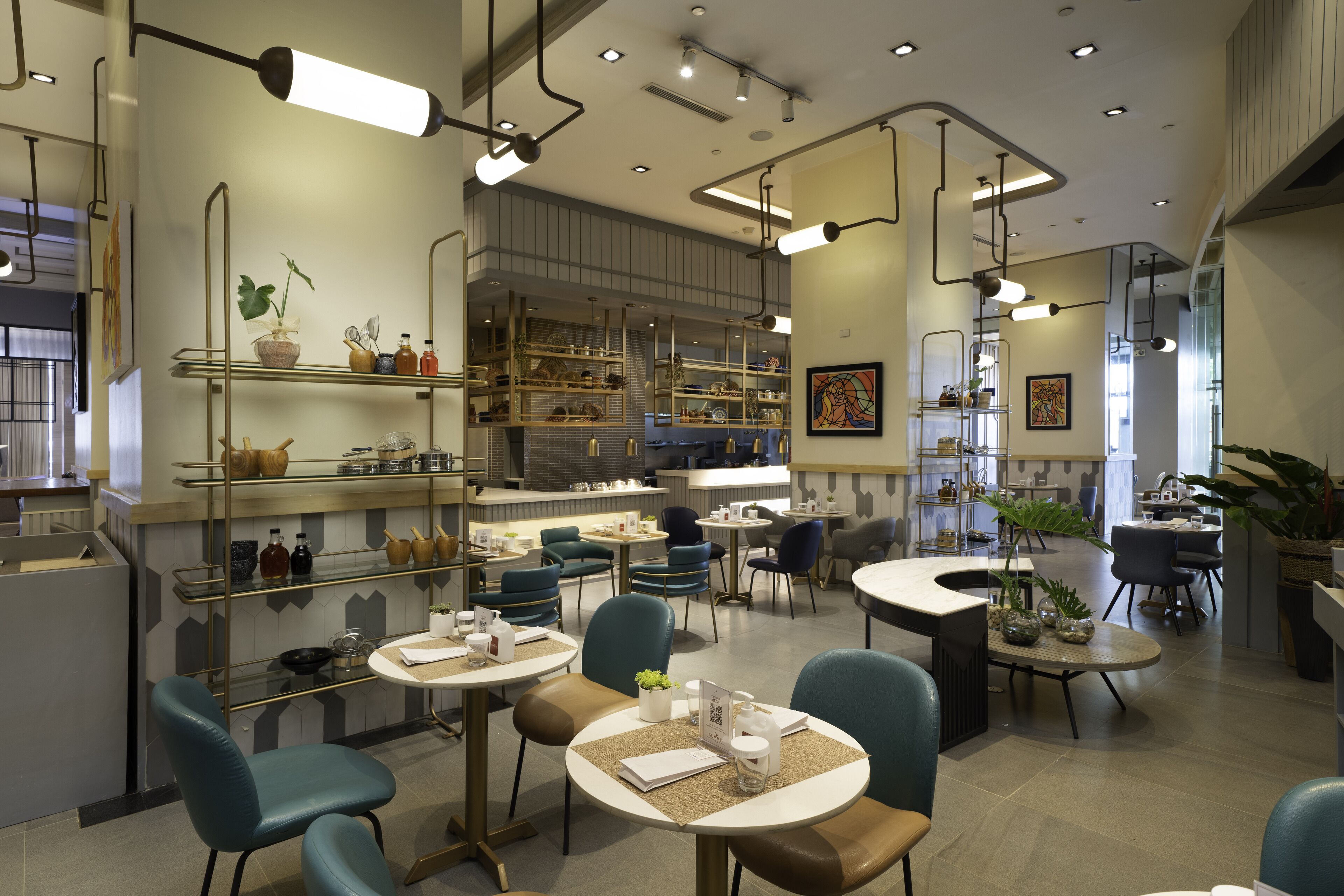 A modern restaurant interior with teal chairs, round tables, and a variety of dishes displayed on shelves.