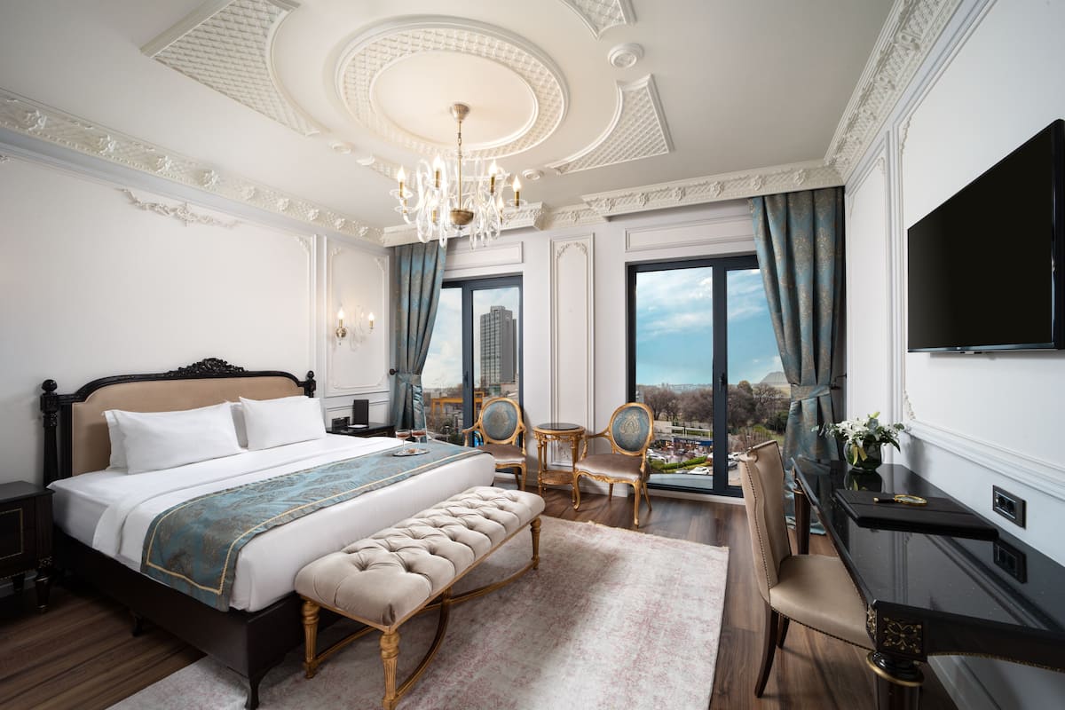 A luxurious bedroom with a large bed, a bench, a desk, and a TV.