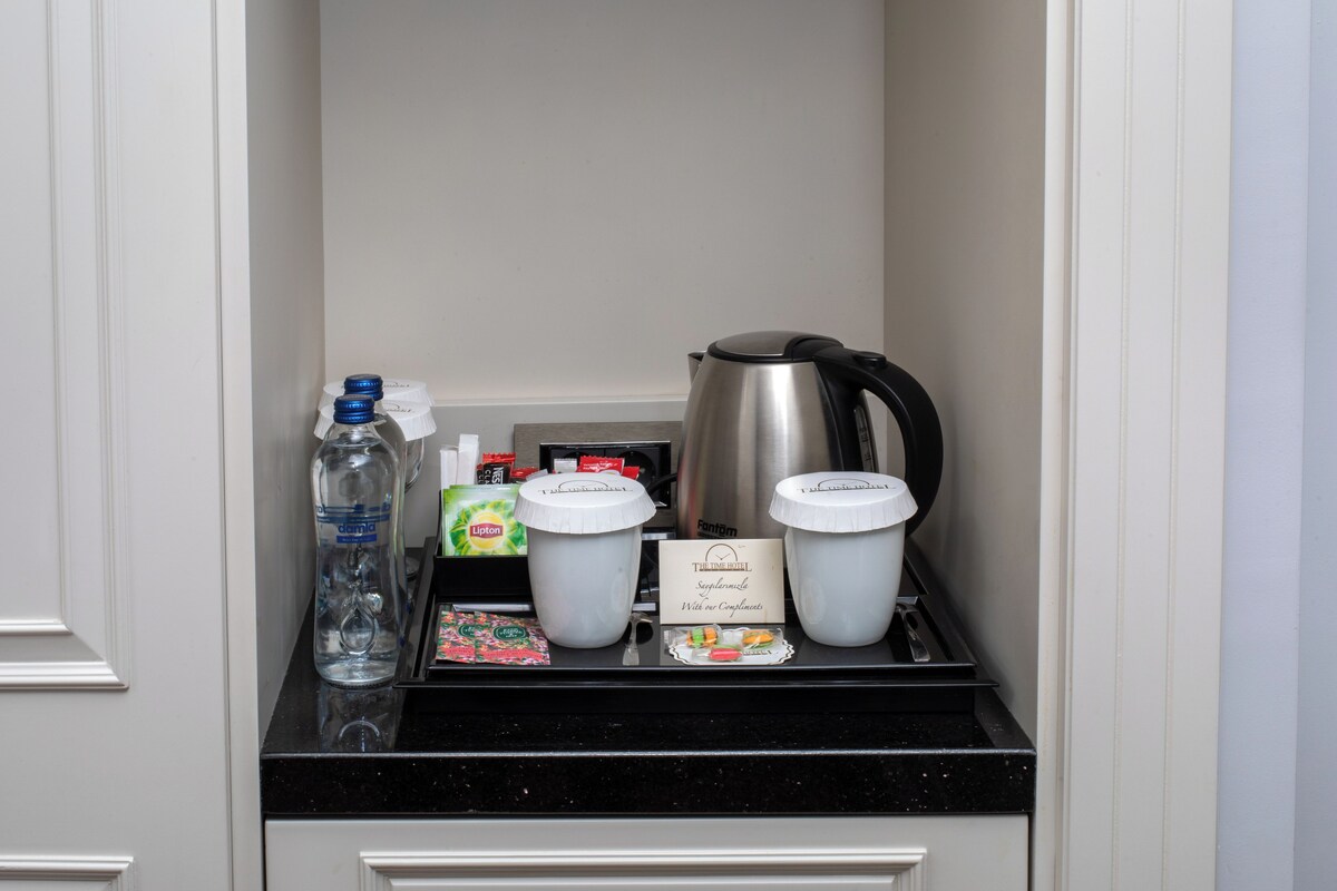 Un minibar con una botella de agua, dos recipientes de café, una bolsita de té y una tetera.