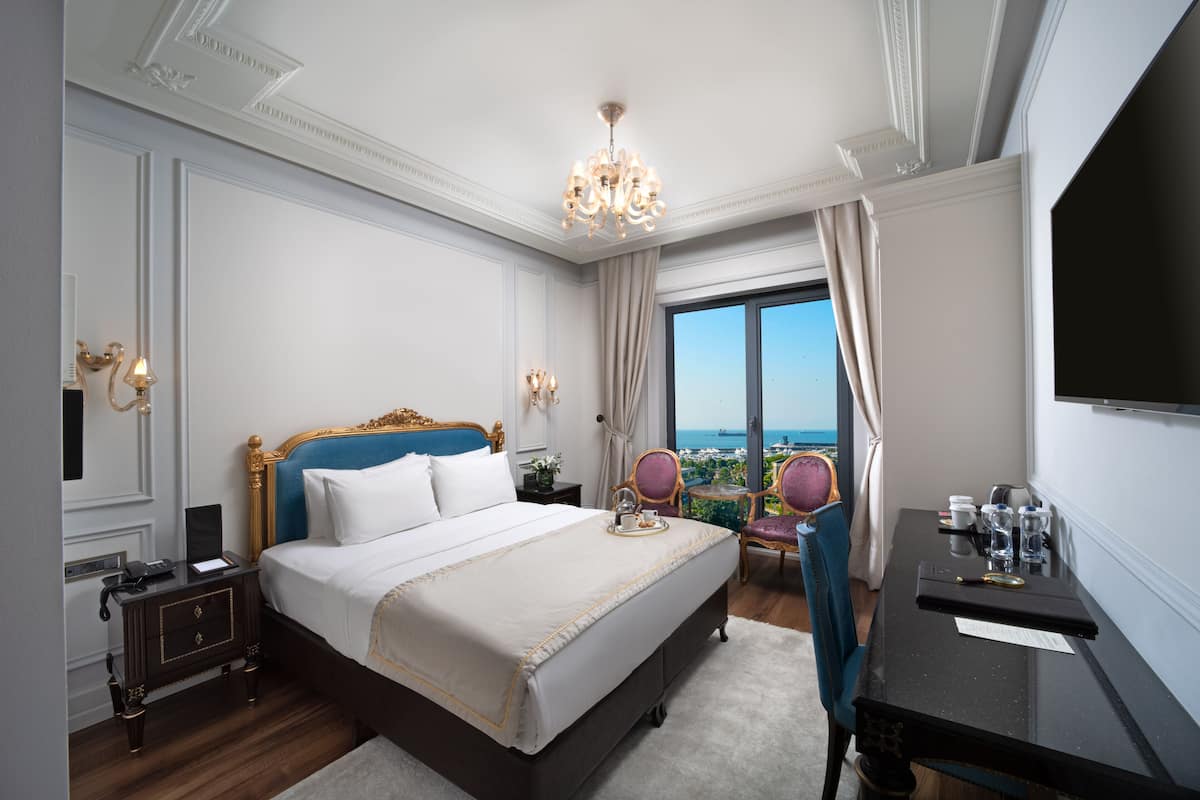 A hotel room with a large bed, a desk with a chair, a television, and a view of the city.