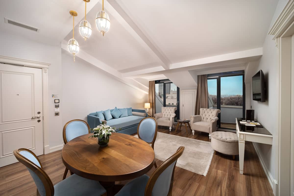 A modern living room with a dining area, featuring a wooden dining table, blue chairs, a sofa, and a TV on a stand.