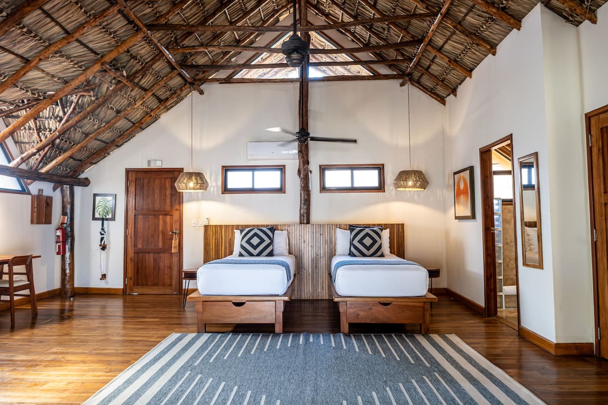 A room with two beds, wooden floors, a sloped ceiling, and a ceiling fan.