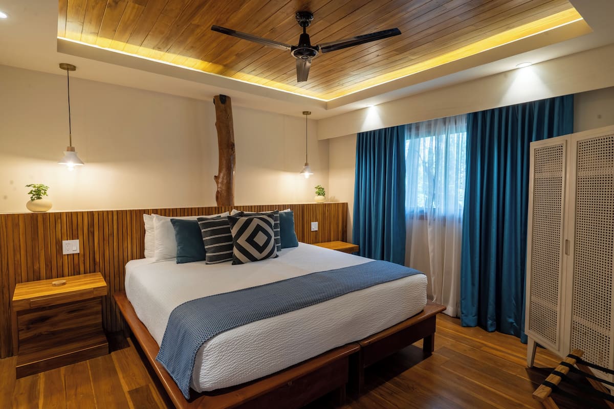 A modern bedroom with a wooden ceiling, a large bed with a blue and white bedspread, two bedside tables with lamps, and a wardrobe.