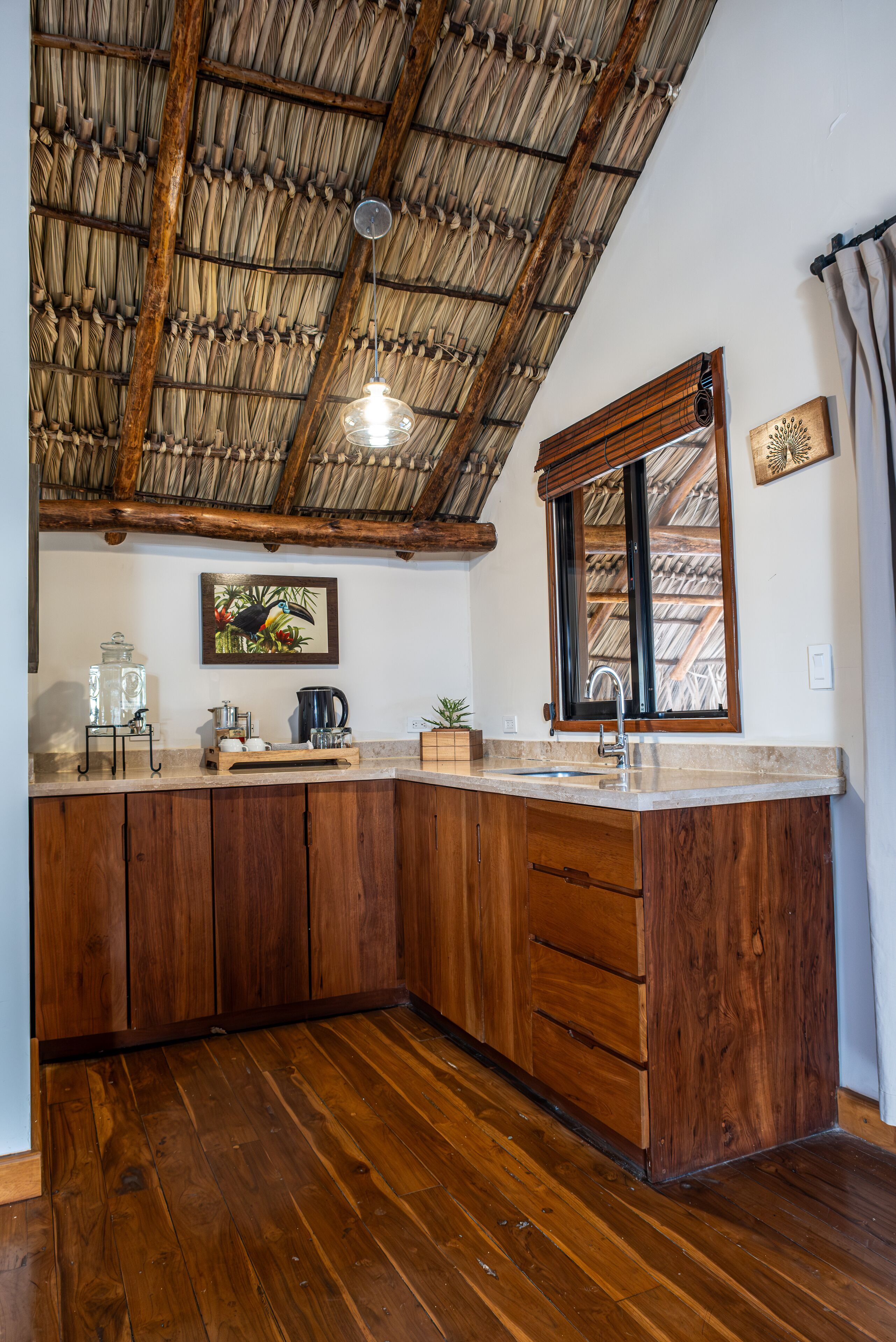 A kitchen with wooden cabinets, a large window, and a hanging light fixture.