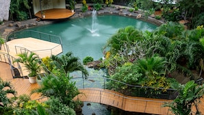 Un jardin intérieur luxuriant avec un bassin central, des allées en bois et un espace aménagé pour s’asseoir.