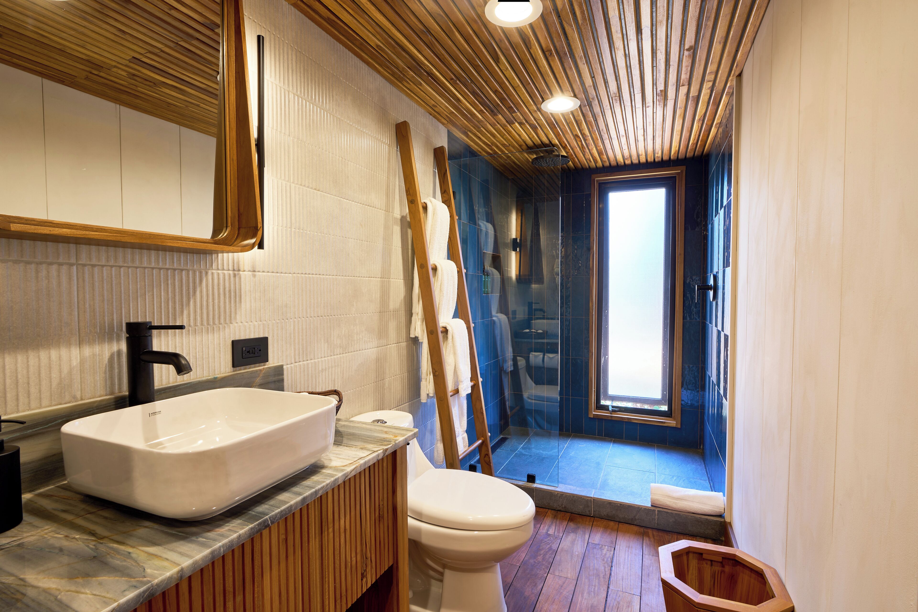 Un baño moderno con un lavamanos tipo recipiente, un inodoro y una escalera de madera apoyada en la pared.