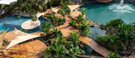Un resort con una piscina grande, una cascada y una estructura de techo de paja.