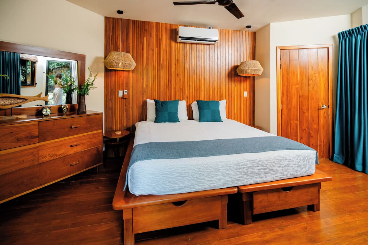 A bedroom with a wooden bed, a wooden dresser, a mirror, and an air conditioning unit on the wall.