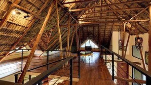 Une structure en bois aux plafonds hauts, dotée d’un toit de chaume, d’un escalier et offrant une vue sur l’intérieur.